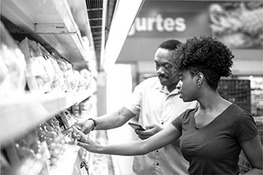A man and a woman are seen looking at produce in the fresh produce aisle in a supermarket.