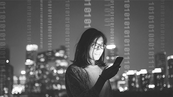 A woman looks at a mobile device she holds in her hand. A lit up city skyline is seen in the background. Columns of one and zeros are seen through the background.
